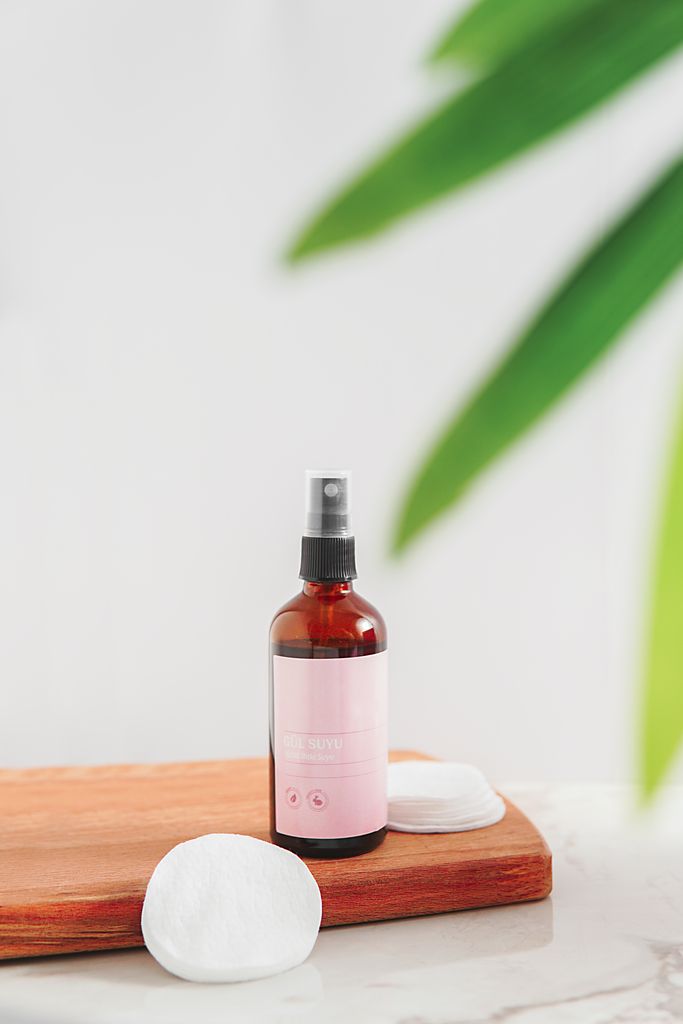 Elegant skincare bottle on a wooden board with cotton pads and green leaves